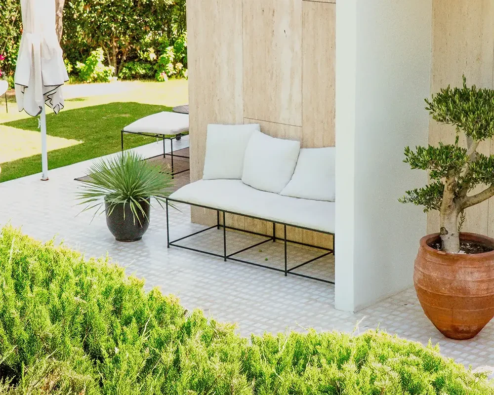 Sofá de exterior sobre pavimento cementoso decorativo con planta en maceta.