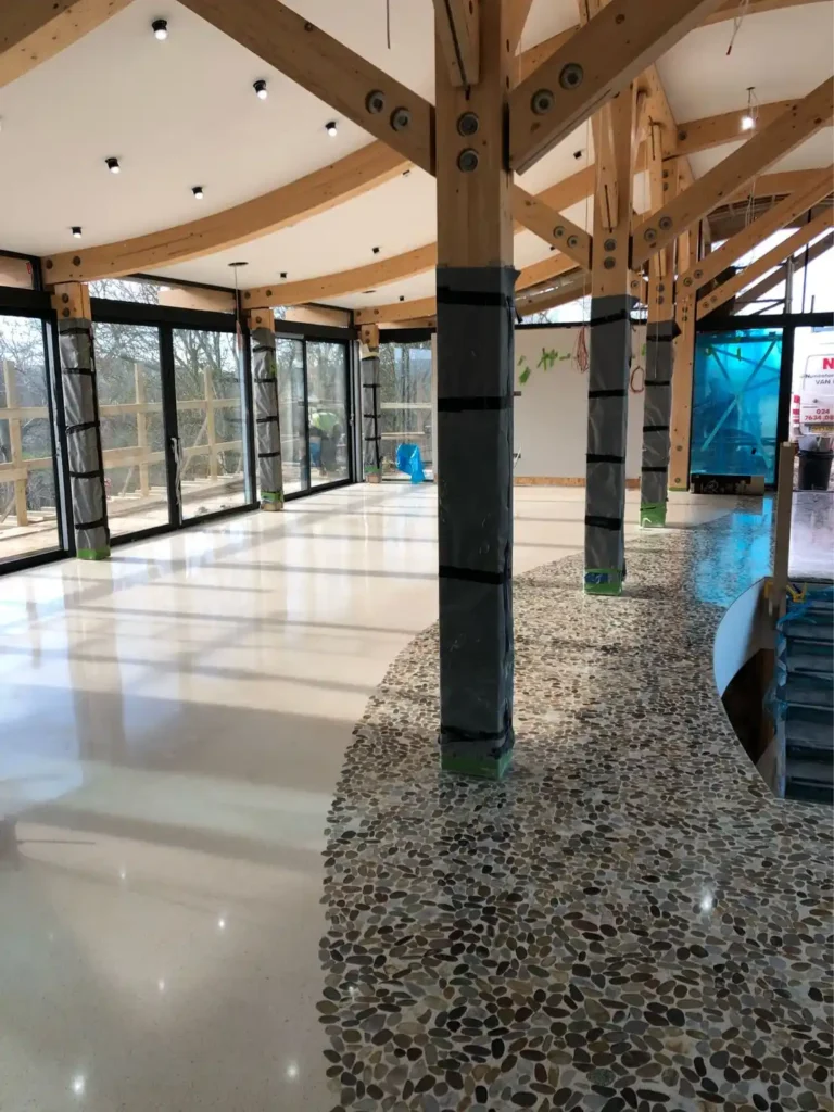 Sala en construcción con estructura de madera visible y suelo de terrazo en tonos beige y piedra.