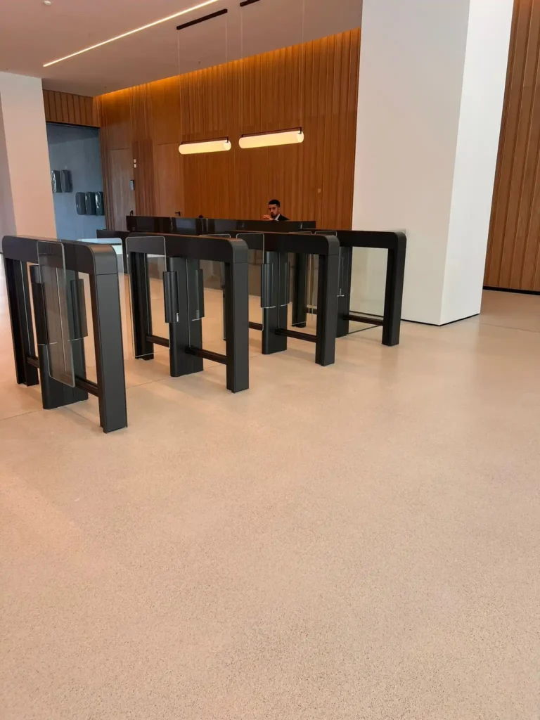 Recepción moderna con puertas de vidrio, turnstiles y paredes de madera en tonos cálidos, con luz ambiental.
