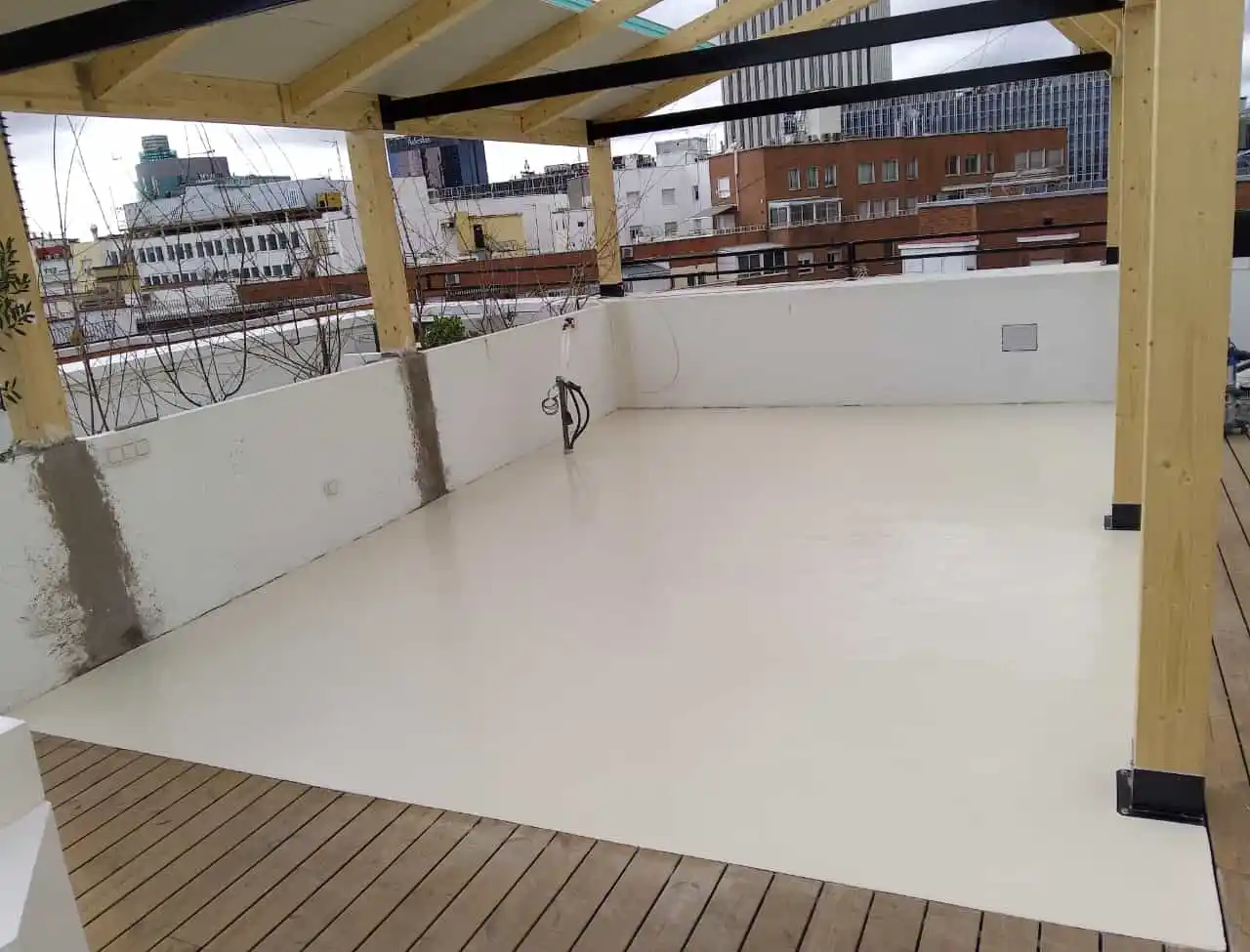 Terraza con piso de cemento blanco y pérgola de madera en entorno urbano.