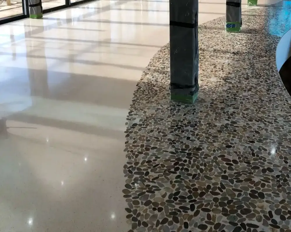 Suelo de terrazo con detalles de piedras naturales en tonos beige y marrón, rodeando columnas en construcción.