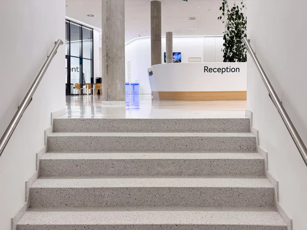 Escalera de pavimento blanco con barandilla y área de recepción visible
