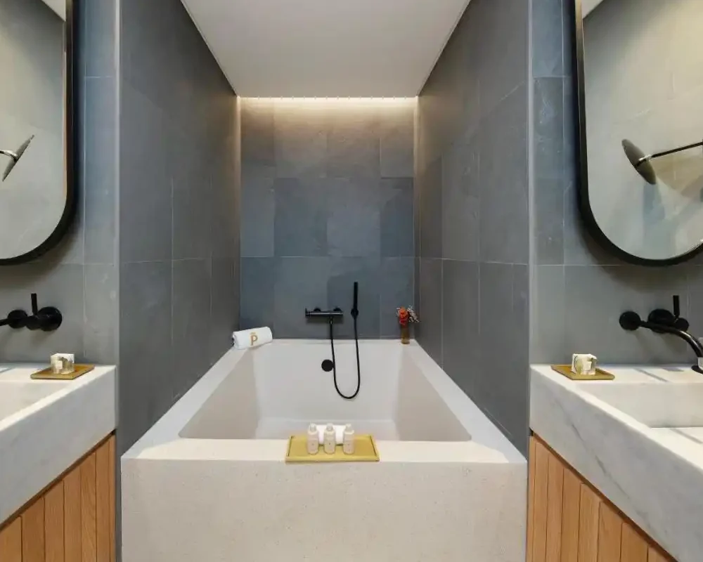 Baño elegante con pavimento cementoso decorativo tipo terrazo, bañera y lavamanos modernos.