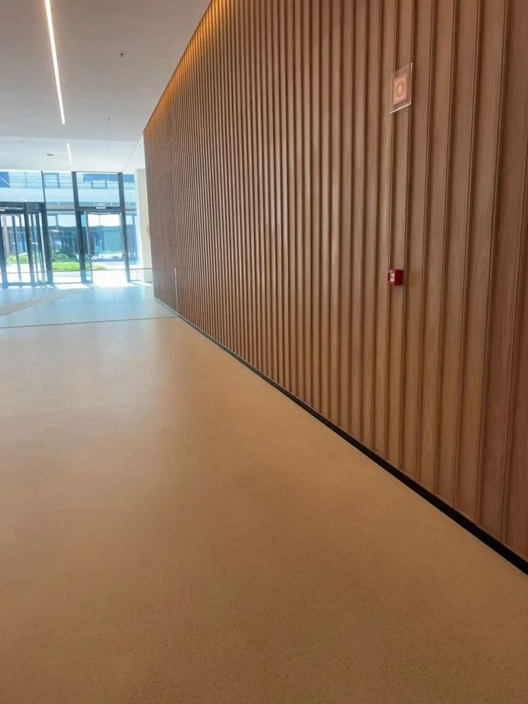 Espacio interior con pared de madera vertical, suelo claro y grandes ventanales.