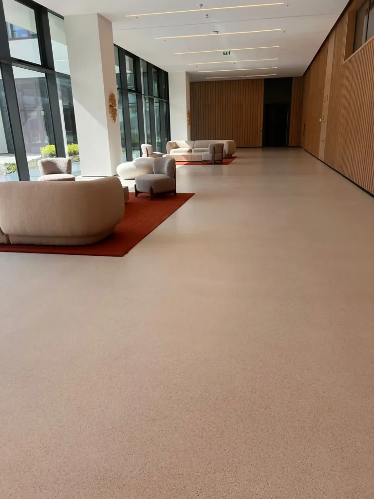Sala de espera con sofás modernos y alfombra roja, rodeada de ventanas grandes con luz natural.