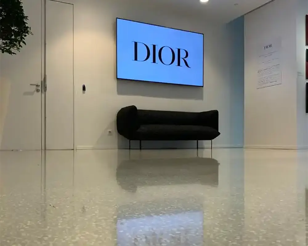 Pantalla digital de Dior en una pared junto a un banco elegante, con reflejo en el suelo pulido.