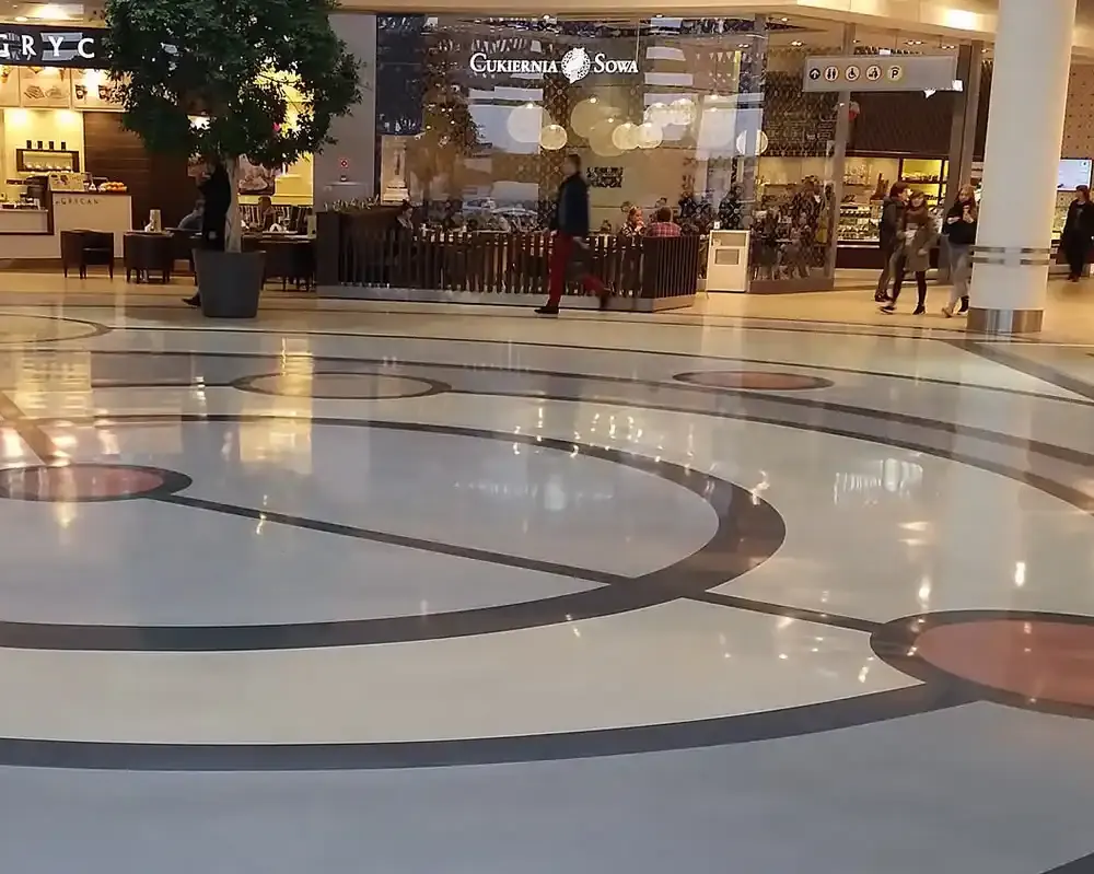 Piso de mármol con diseño circular y caminos que conectan diferentes áreas en un centro comercial moderno.