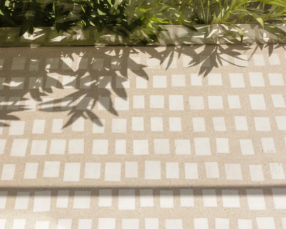 Mosaico de cerámica con sombras de plantas, ideal para suelos y decoración exterior.