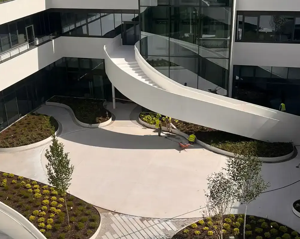 Vista de patio interior con escaleras de diseño moderno, jardines y trabajadores en la zona de construcción.
