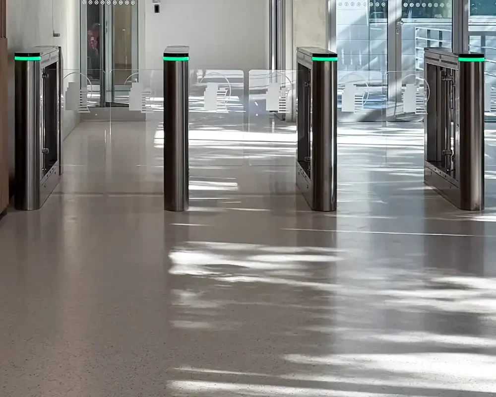 Entrada a edificio moderno con pavimento cementoso decorativo y torniquetes automáticos.