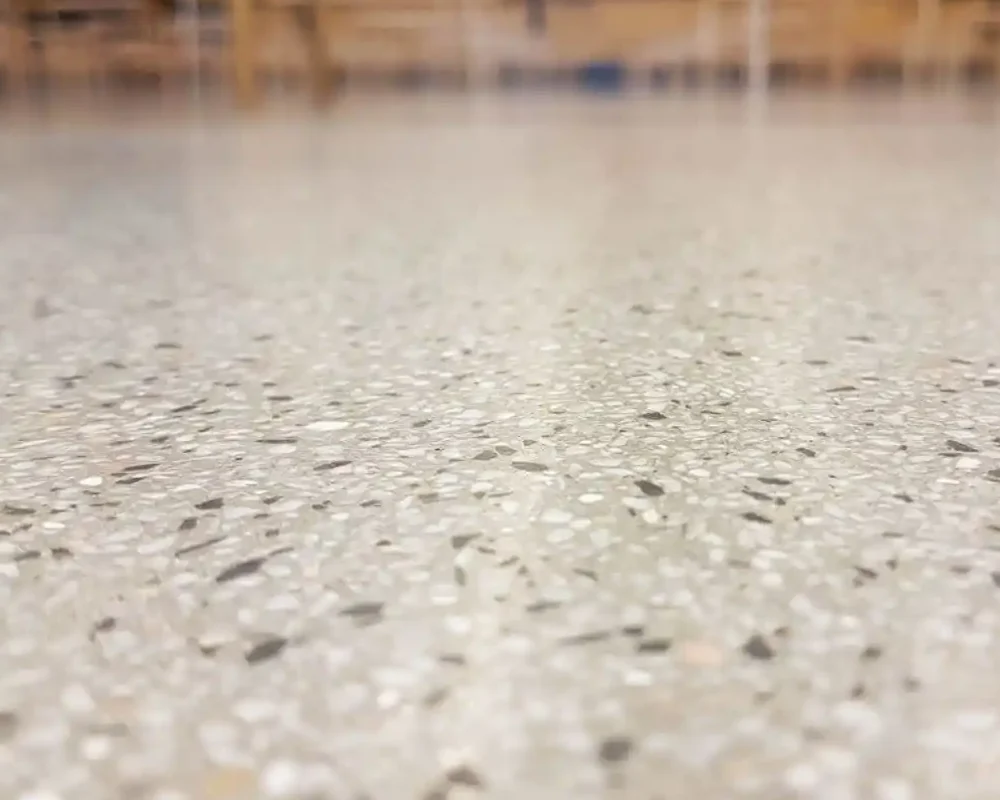 Suelo de terrazo con mesas al fondo, en un ambiente amplio y bien iluminado.