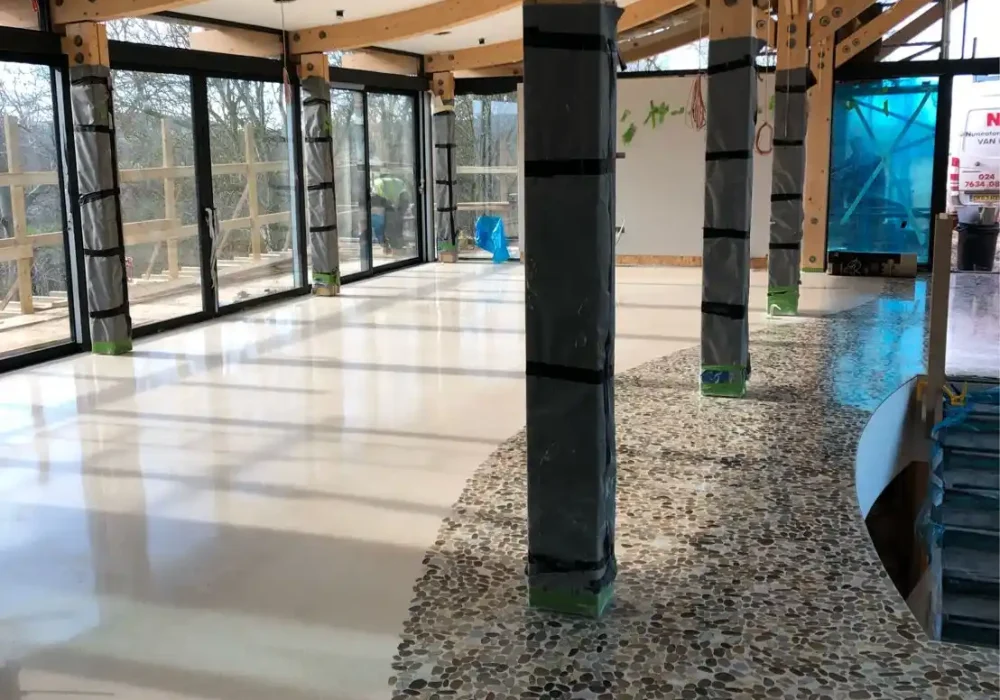 Sala en construcción con estructura de madera visible y suelo de terrazo en tonos beige y piedra.