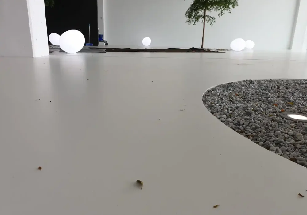 Piso de terrazo blanco con detalles de grava en una zona exterior con iluminación moderna.
