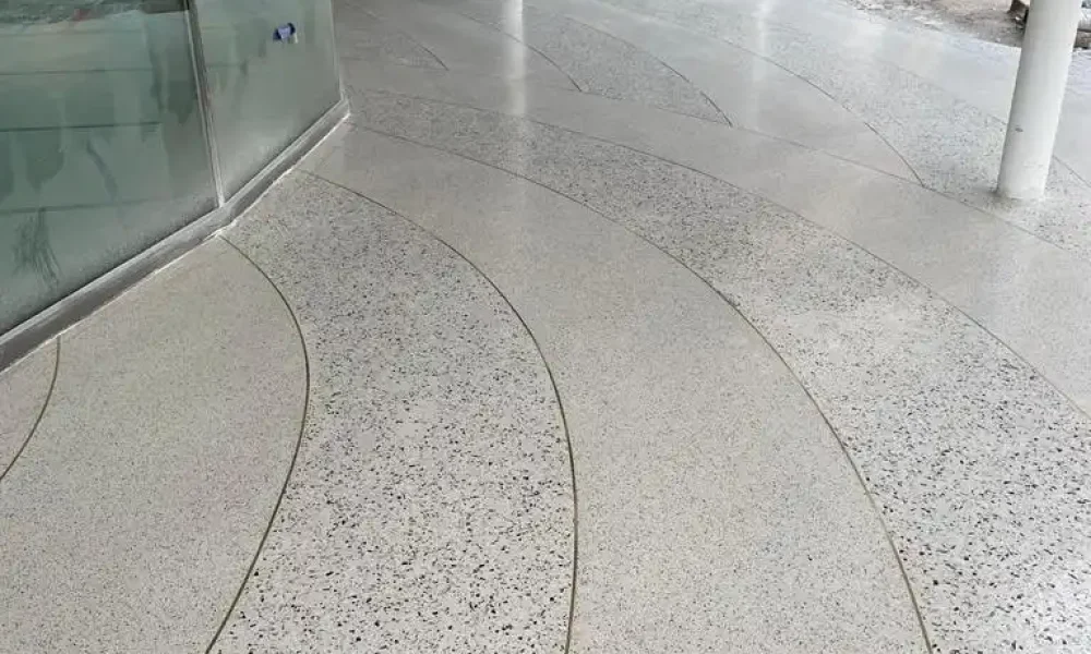 Suelo de terrazzo blanco con líneas doradas en el centro de un edificio en construcción, con grandes ventanales.