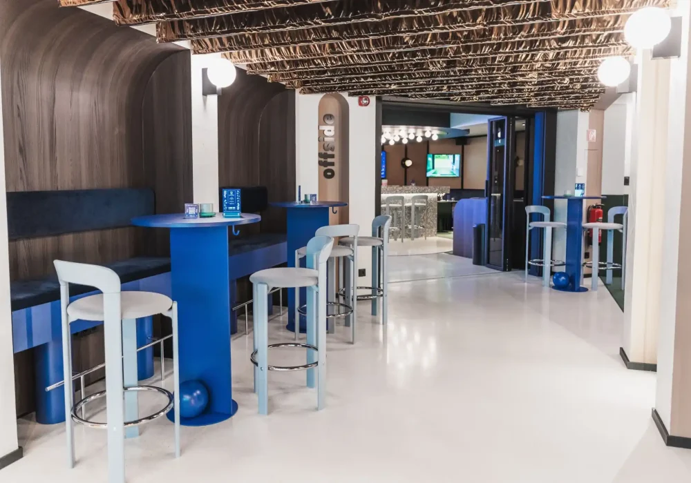 Espacio moderno de bar con mesas y sillas de colores vibrantes y suelo de terrazo blanco.